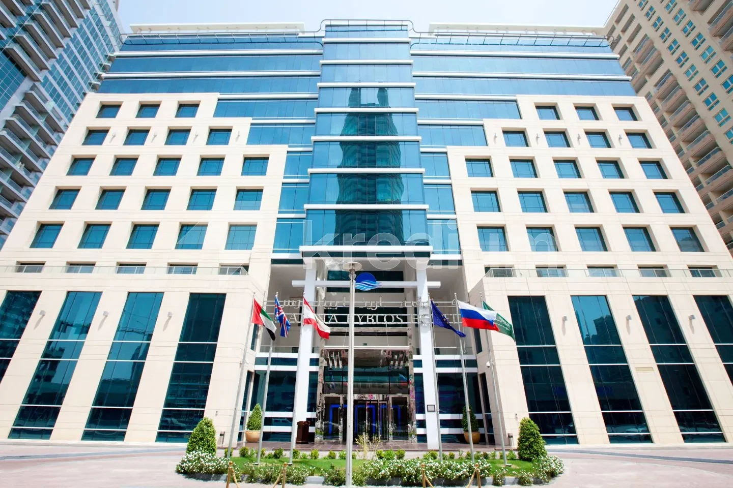 Entrance to a modern hotel with flags and greenery in front of it