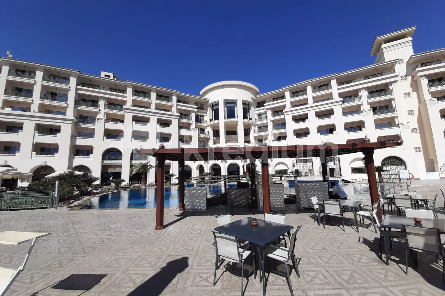 A white mid-rise building with a cafe and a swimming pool in front of it