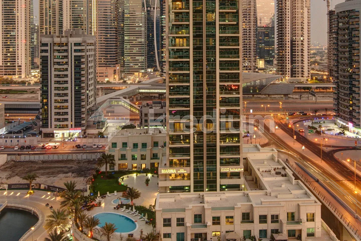 A night image of an elegant skyscraper surrounded by busy roads, a pool and a bay