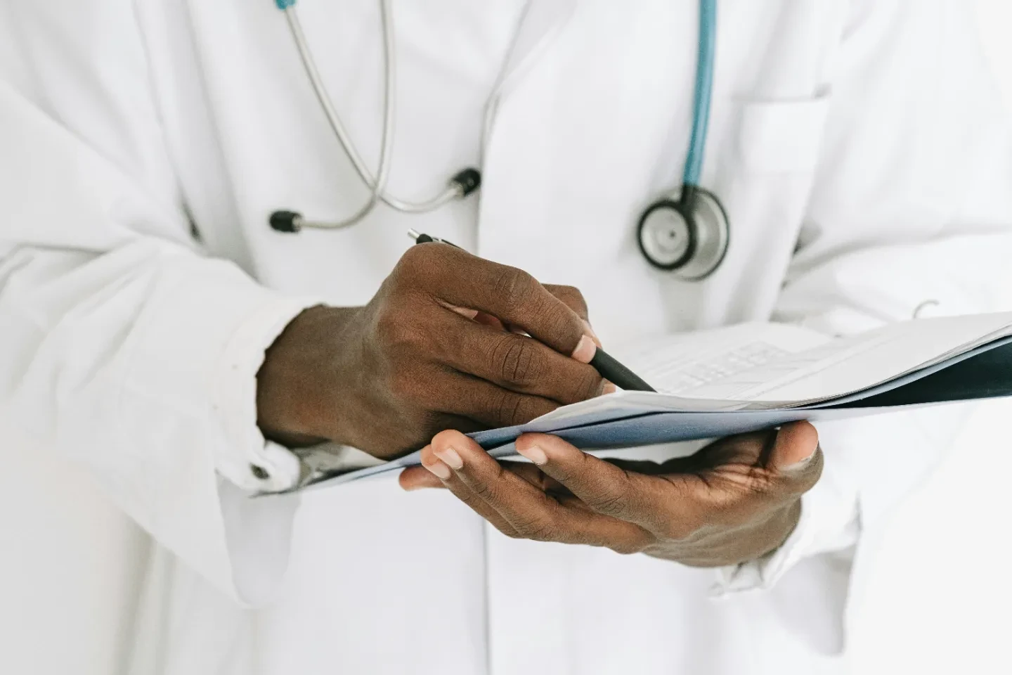 Hands of a person with stethoscope writing in documents.