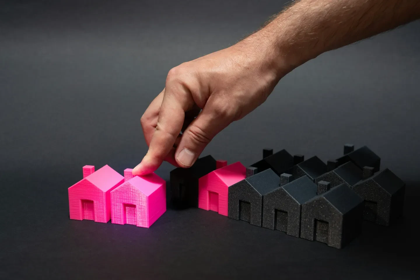 A hand moving two pink house figures to the front.