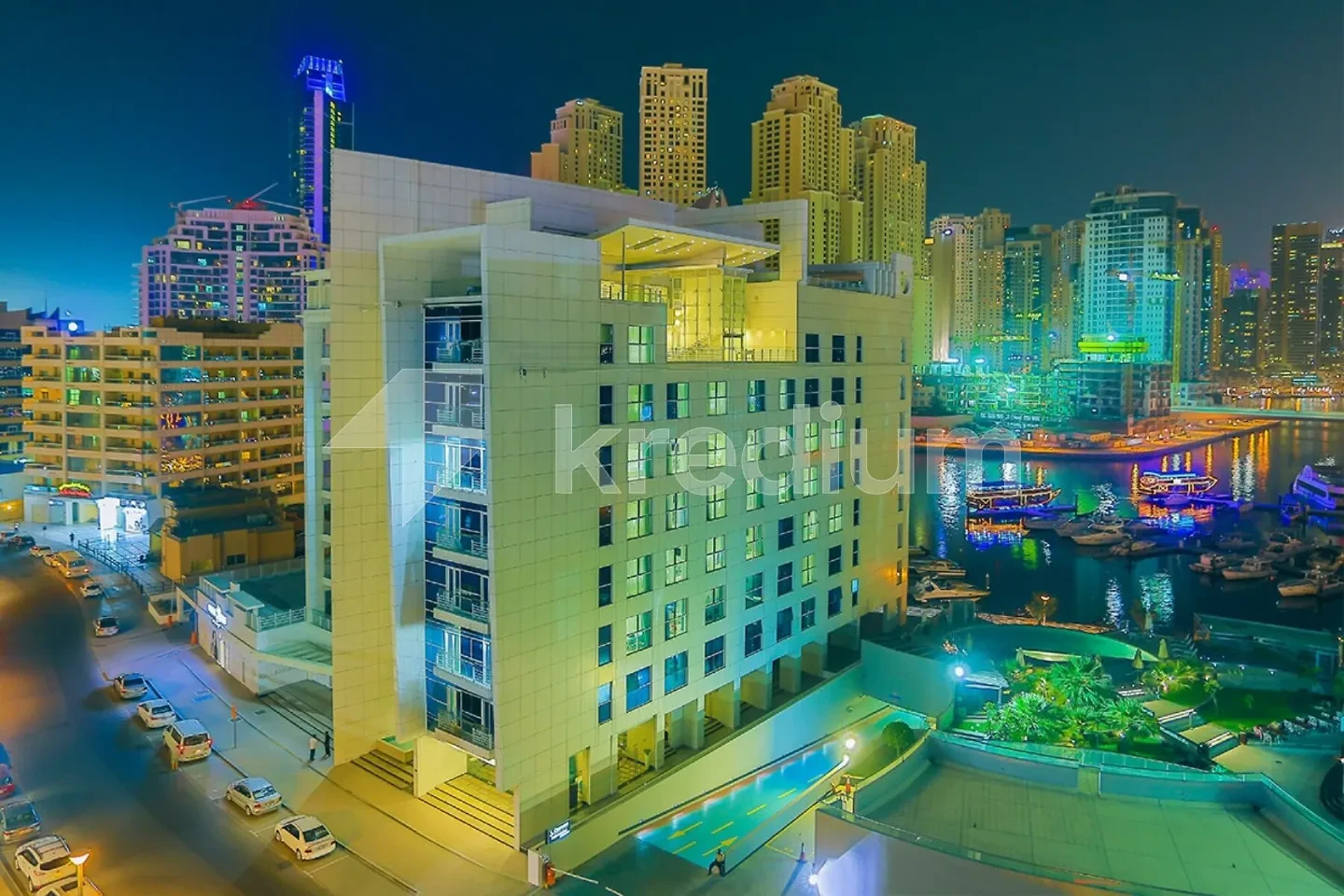 A night image of a modern mid-rise building with a port in the background
