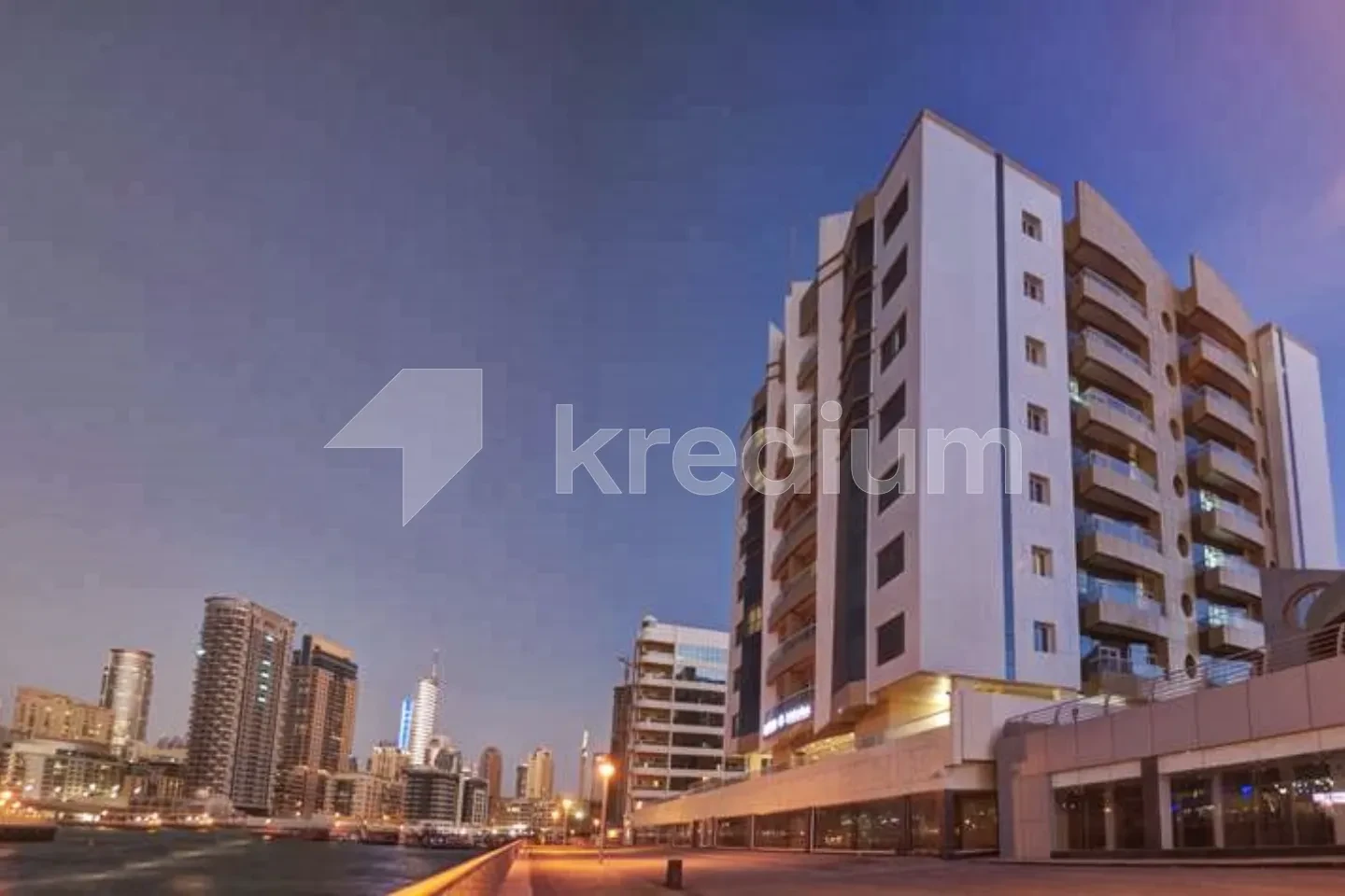 A night image of a mid-rise hotel building next to a canal