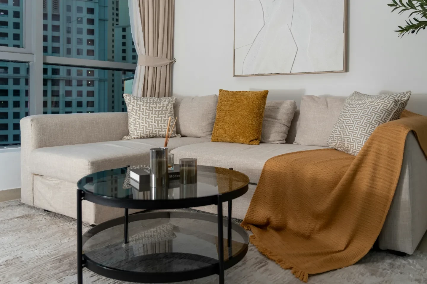 A round coffee table and couch with pillows and orange throw in an apartment.