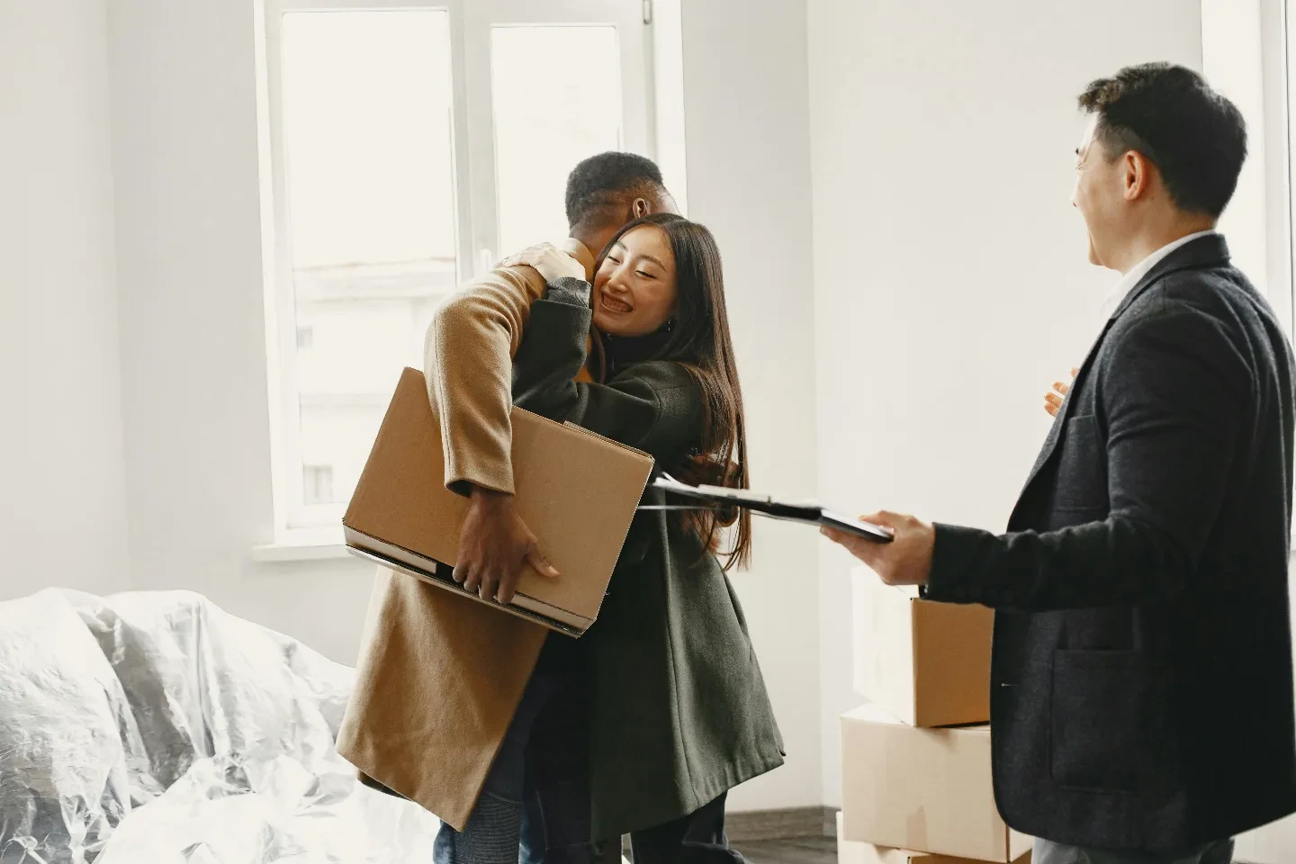 A real estate agent looking at a couple hugging each other.