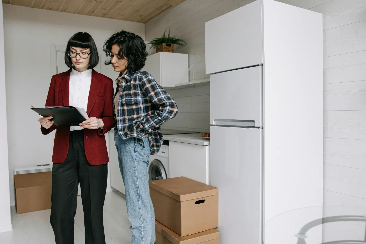 A real estate agent in a suit with a woman to the right standing in an apartment, both looking at the document.