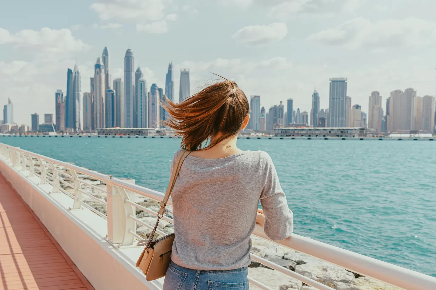 A woman looking at the city of Dubai across the sea.