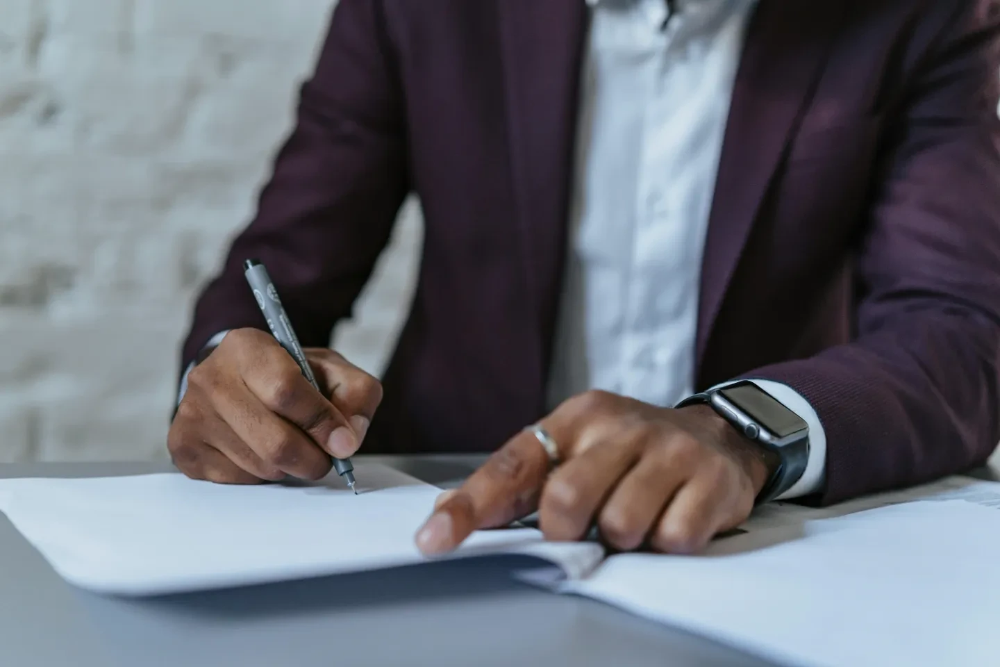 A person in a suit with a smartwatch, writing in a document.