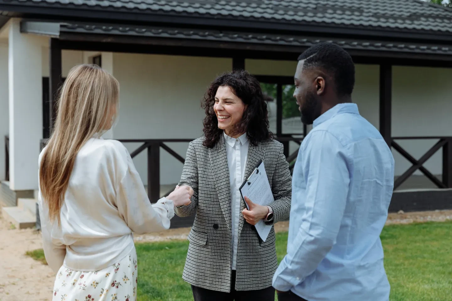 A man looking at two women shaking hands in front of a house.