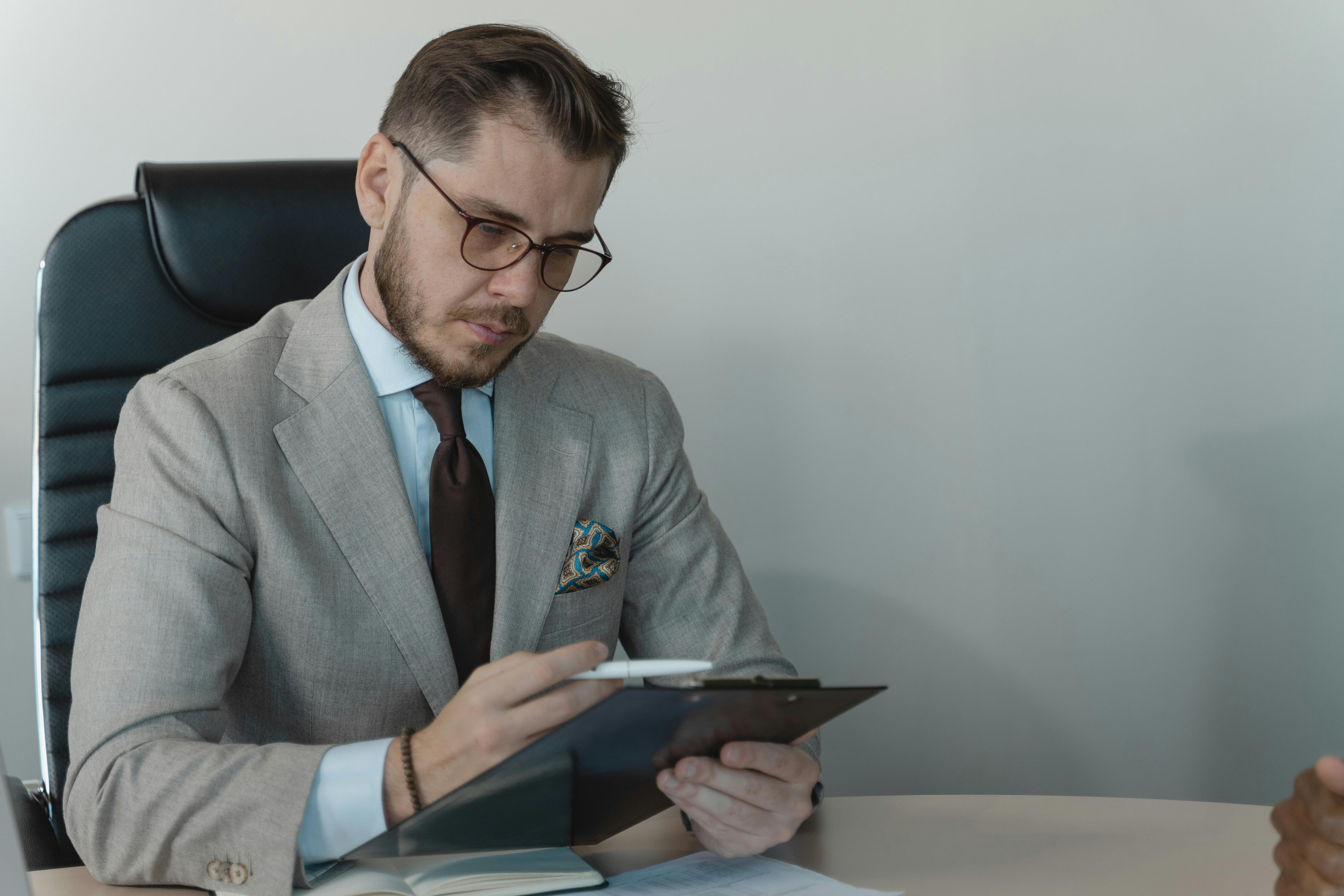 A man in a suit with glasses looking at a document.