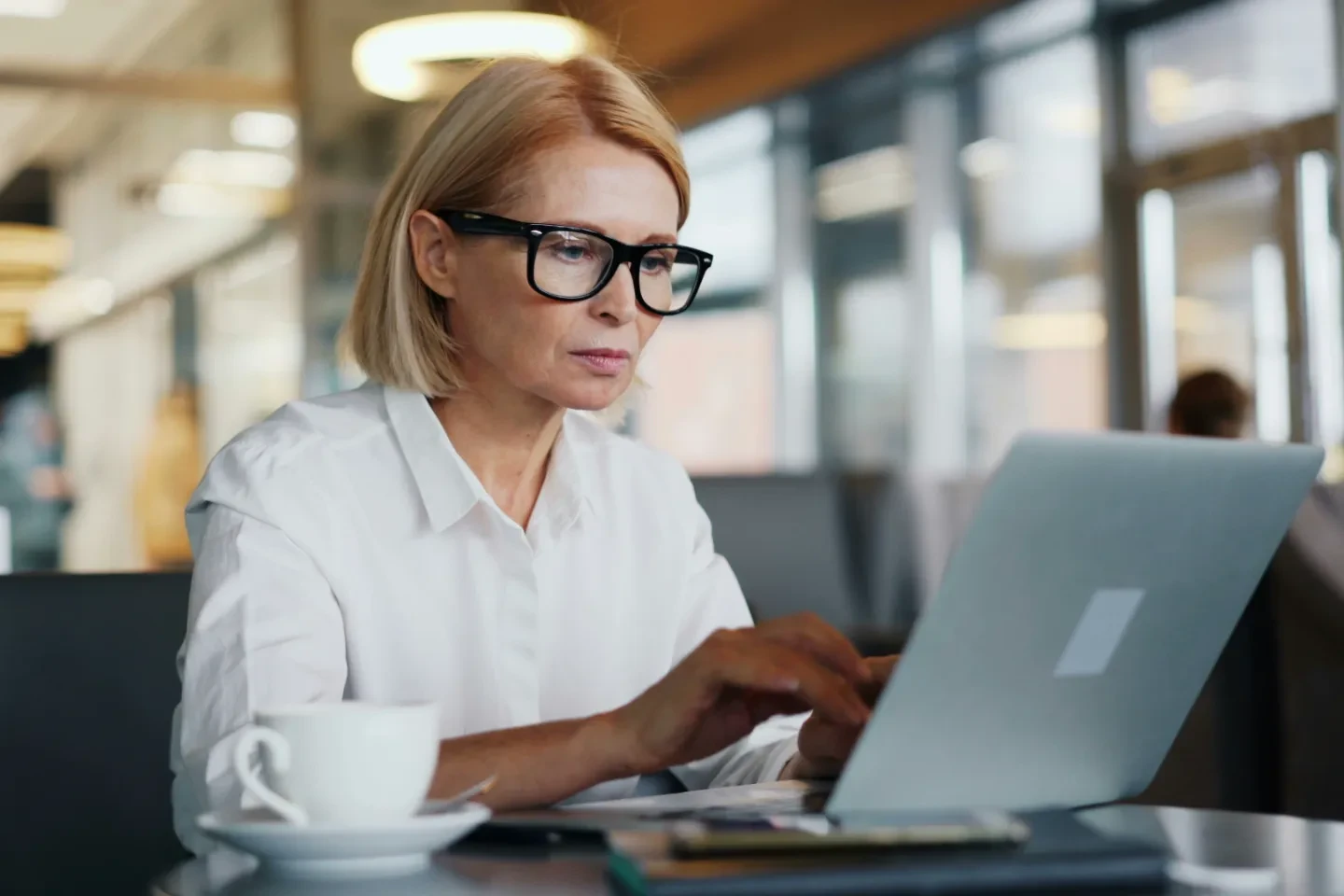 A woman with glasses typing on a laptop.