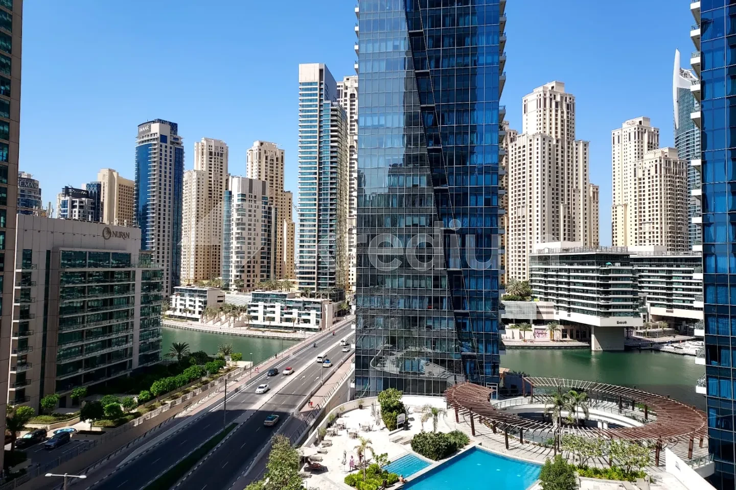 A glass skyscraper overlooking a canal and a busy road
